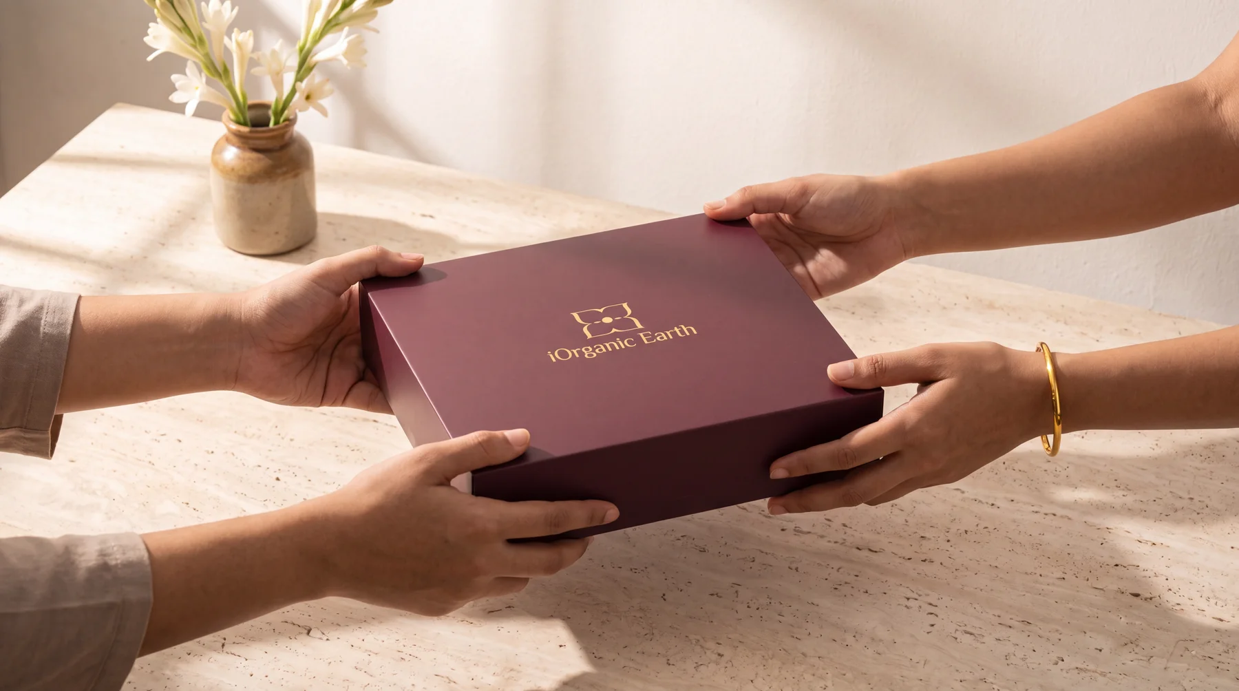 Two people passing a maroon iOrganic Earth gift box across a travertine table